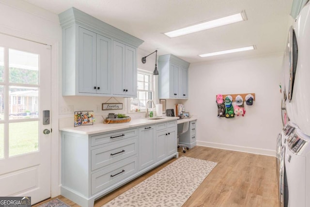 kitchen with sink, light wood-type flooring, stacked washing maching and dryer, and a healthy amount of sunlight