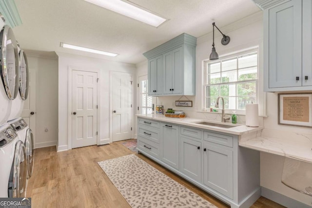 kitchen with light wood-type flooring, washer / clothes dryer, light stone counters, pendant lighting, and sink