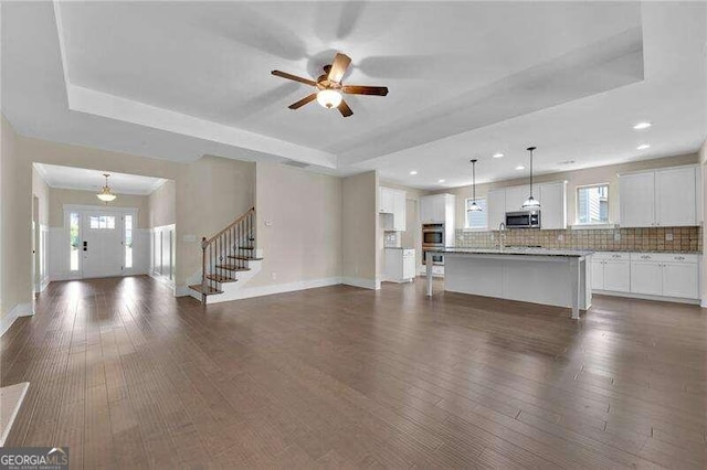 unfurnished living room with a raised ceiling, ceiling fan, and dark hardwood / wood-style floors