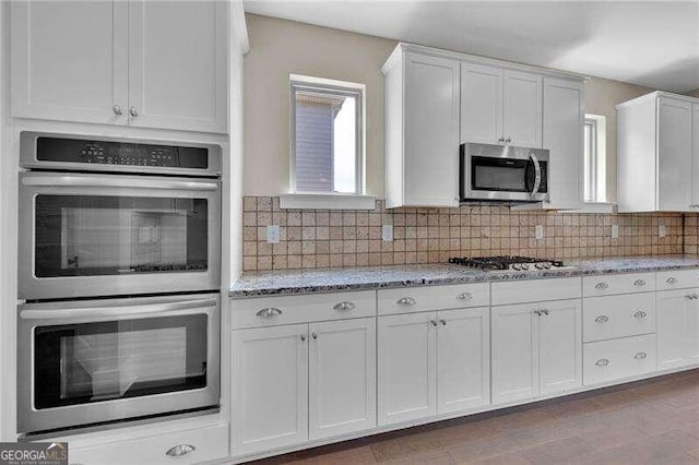 kitchen featuring light stone countertops, white cabinetry, tasteful backsplash, wood-type flooring, and appliances with stainless steel finishes