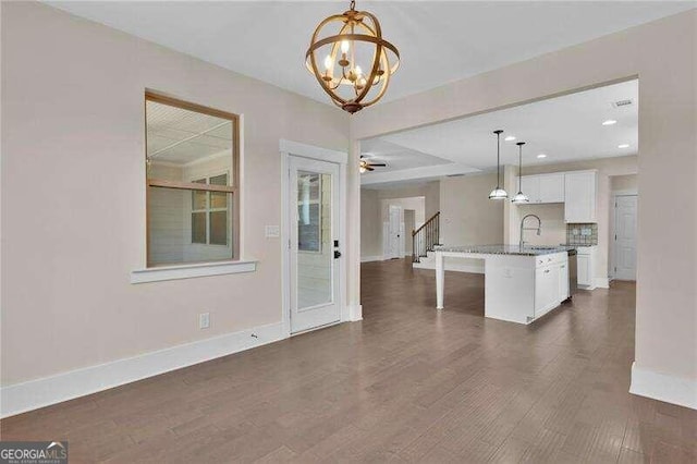 kitchen featuring white cabinetry, dark wood-type flooring, a kitchen breakfast bar, an island with sink, and pendant lighting