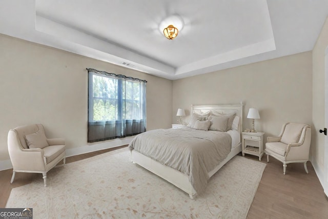 bedroom with a tray ceiling and light hardwood / wood-style flooring