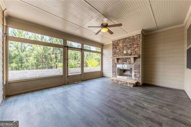 unfurnished living room with ceiling fan, a stone fireplace, wood-type flooring, wooden walls, and ornamental molding