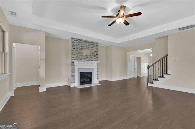 unfurnished living room with a fireplace, a tray ceiling, ceiling fan, and dark wood-type flooring