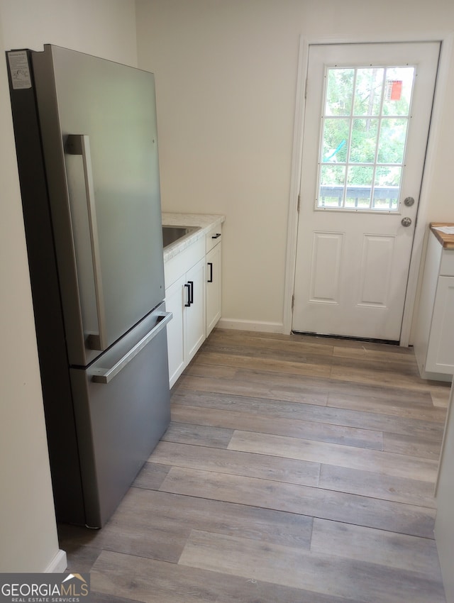 kitchen featuring white cabinets, light hardwood / wood-style flooring, stainless steel refrigerator, and sink