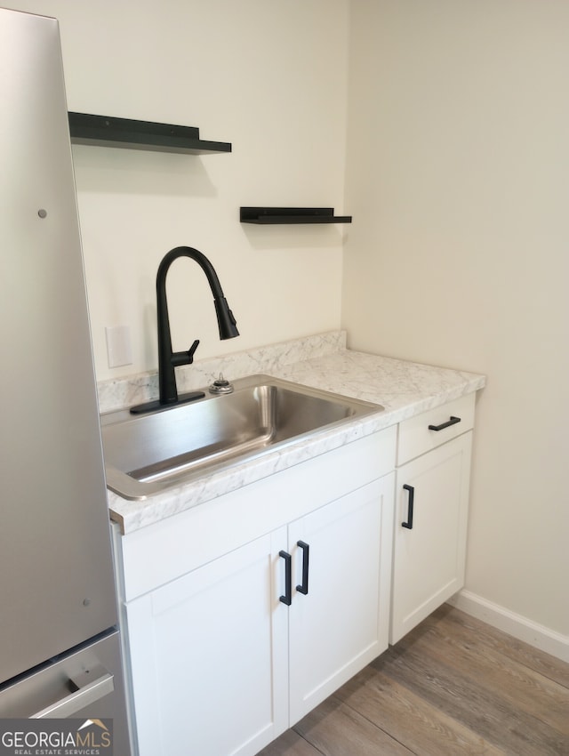 kitchen with stainless steel fridge, sink, light stone countertops, white cabinetry, and wood-type flooring