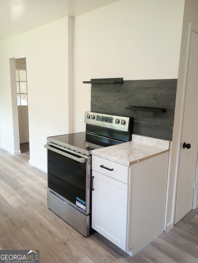 kitchen featuring stainless steel range with electric stovetop, light stone counters, white cabinets, and light hardwood / wood-style floors