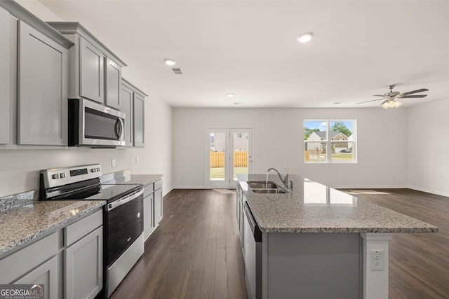 kitchen with appliances with stainless steel finishes, an island with sink, sink, gray cabinetry, and light stone counters