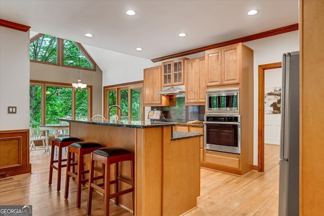 kitchen with dark stone countertops, appliances with stainless steel finishes, light wood-type flooring, and a kitchen bar