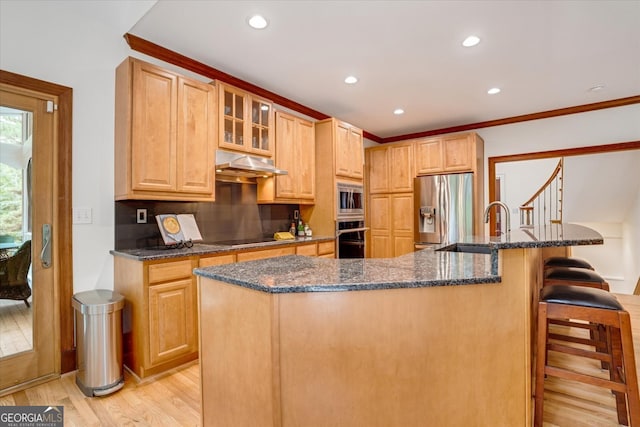 kitchen with dark stone countertops, light wood-type flooring, a kitchen island with sink, stainless steel appliances, and a kitchen breakfast bar