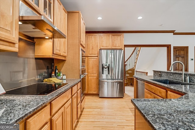 kitchen with dark stone counters, wall chimney exhaust hood, sink, light hardwood / wood-style floors, and appliances with stainless steel finishes