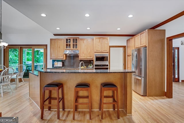 kitchen with dark stone countertops, light hardwood / wood-style flooring, stainless steel appliances, and a breakfast bar