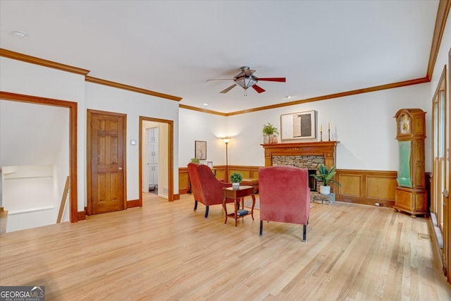 living room with a stone fireplace, light wood-type flooring, ceiling fan, and ornamental molding