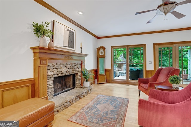 living room featuring a stone fireplace, ceiling fan, light hardwood / wood-style flooring, and crown molding