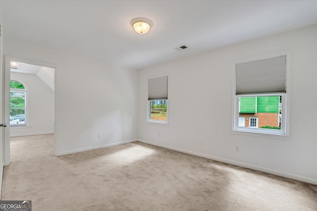 unfurnished room with a healthy amount of sunlight, light colored carpet, and vaulted ceiling