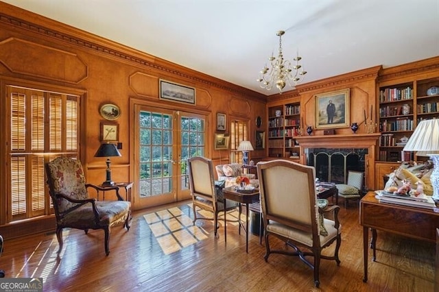 living area with a premium fireplace, built in shelves, wood-type flooring, and a notable chandelier