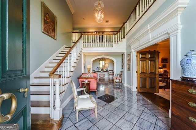 tiled entryway with decorative columns, crown molding, and a towering ceiling