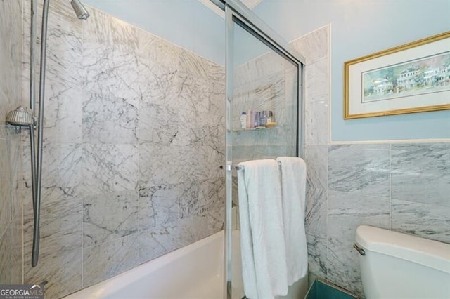 bathroom with toilet, enclosed tub / shower combo, and tile walls