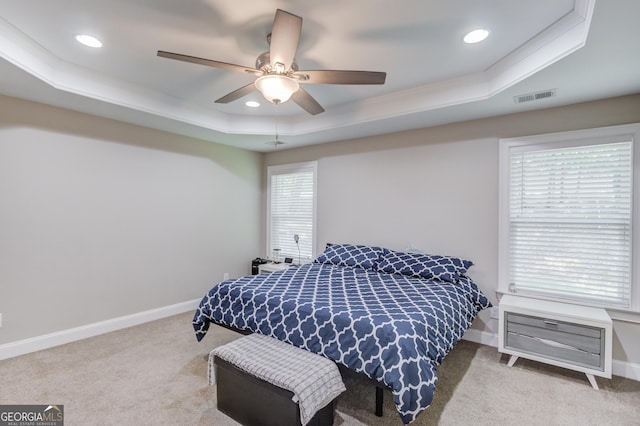 carpeted bedroom with multiple windows, a tray ceiling, crown molding, and ceiling fan