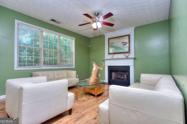 living room featuring wood-type flooring, a textured ceiling, a large fireplace, and ceiling fan