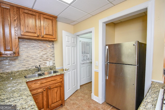 kitchen featuring stainless steel refrigerator, sink, backsplash, light tile patterned floors, and light stone countertops