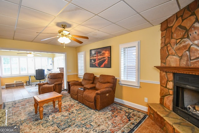 tiled living room with ceiling fan, a drop ceiling, and a fireplace