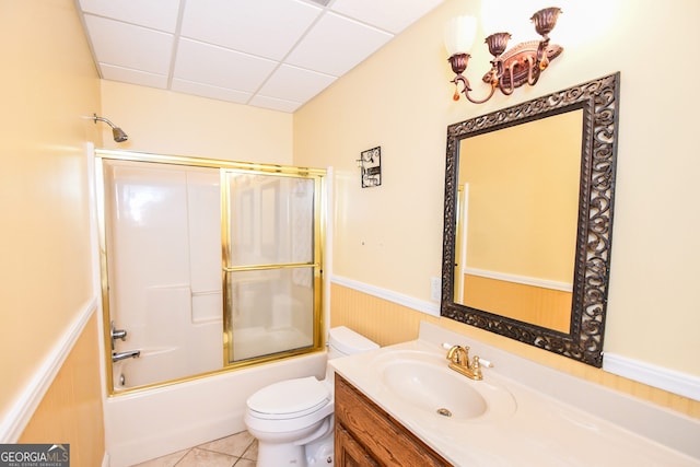 full bathroom with combined bath / shower with glass door, tile patterned flooring, vanity, a drop ceiling, and toilet