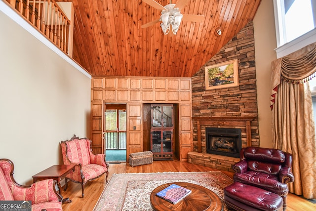 living room with light hardwood / wood-style flooring, ceiling fan, high vaulted ceiling, a stone fireplace, and wooden ceiling