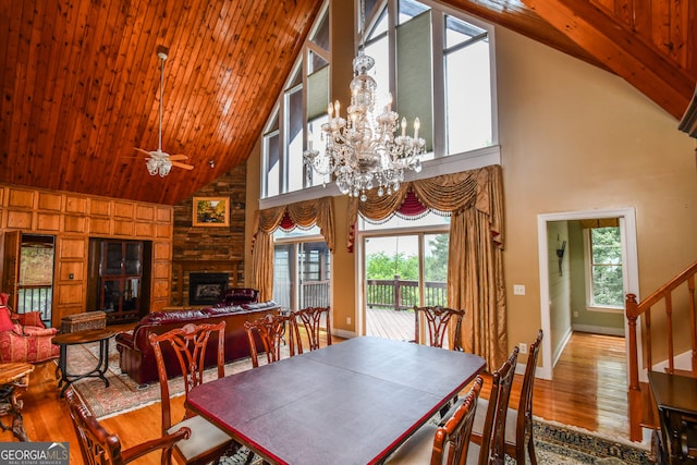 dining room with wood ceiling, high vaulted ceiling, hardwood / wood-style flooring, a fireplace, and ceiling fan with notable chandelier