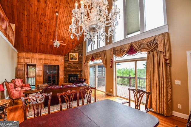 dining space with wood ceiling, high vaulted ceiling, a fireplace, ceiling fan with notable chandelier, and light wood-type flooring