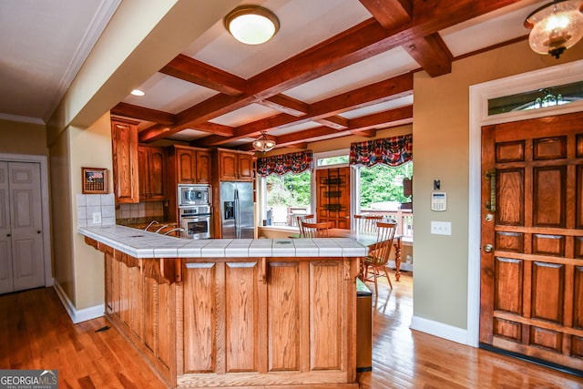 kitchen with stainless steel appliances, coffered ceiling, tile counters, and kitchen peninsula