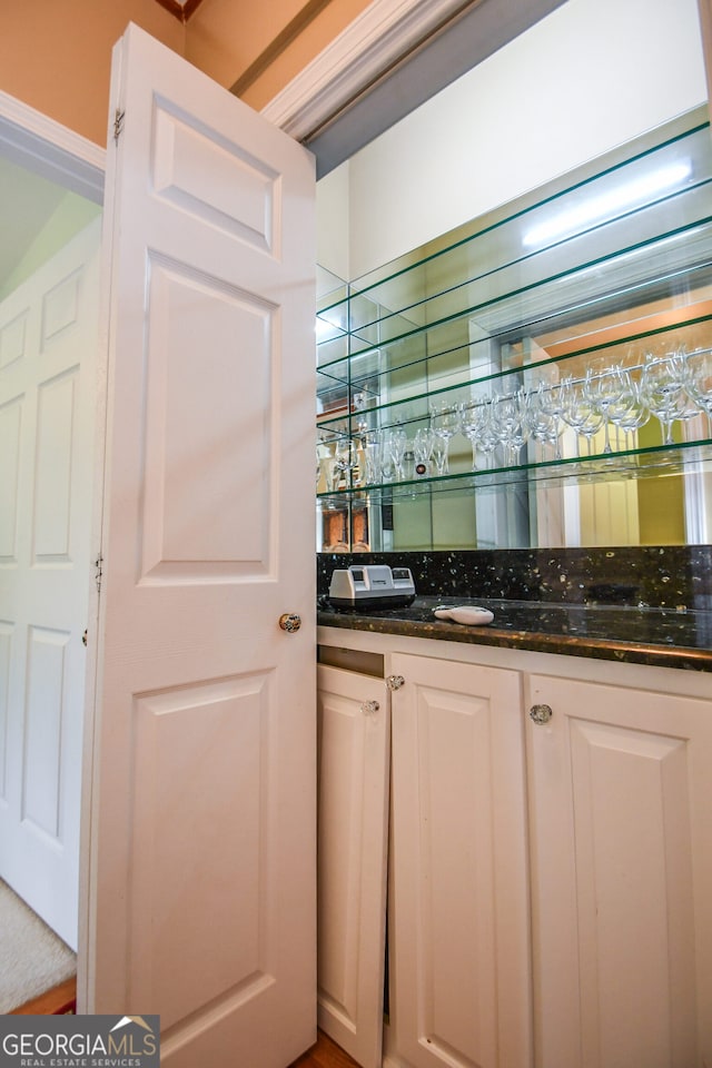 bar featuring dark stone countertops and white cabinets