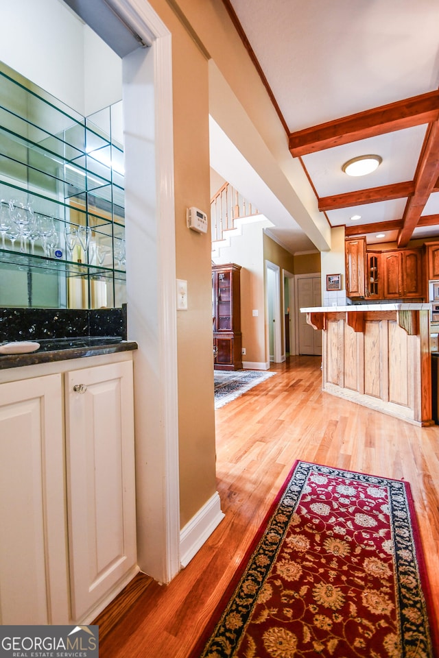 kitchen featuring stainless steel microwave, beamed ceiling, a kitchen breakfast bar, coffered ceiling, and light hardwood / wood-style floors