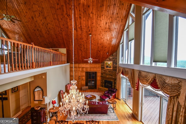 living room with light hardwood / wood-style flooring, ceiling fan, high vaulted ceiling, a stone fireplace, and wooden ceiling