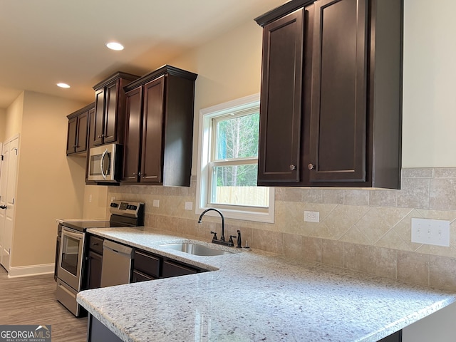 kitchen with dark brown cabinetry, light stone counters, stainless steel appliances, and a sink