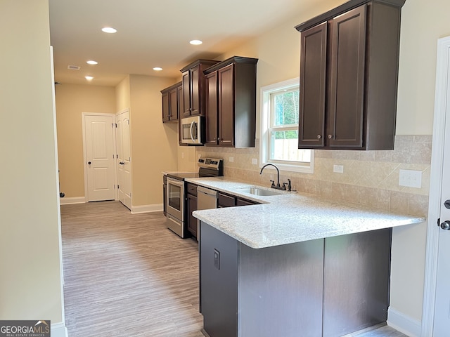 kitchen featuring appliances with stainless steel finishes, a sink, dark brown cabinetry, and light stone countertops