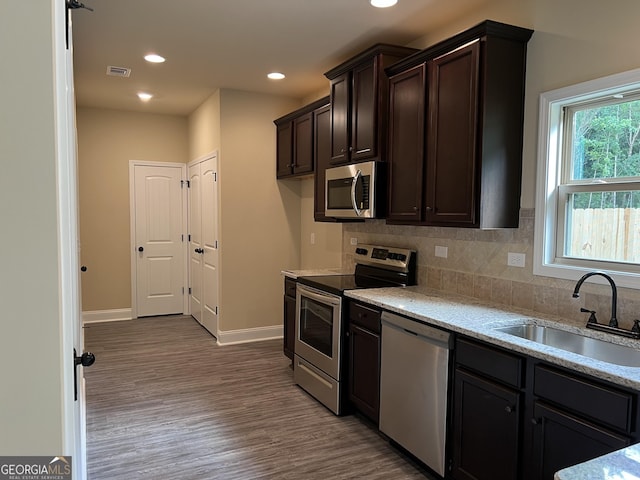 kitchen with backsplash, appliances with stainless steel finishes, a sink, dark brown cabinetry, and wood finished floors