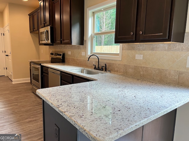 kitchen with wood-type flooring, decorative backsplash, light stone countertops, dark brown cabinetry, and appliances with stainless steel finishes