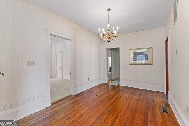 unfurnished room with an inviting chandelier, a textured ceiling, and hardwood / wood-style floors