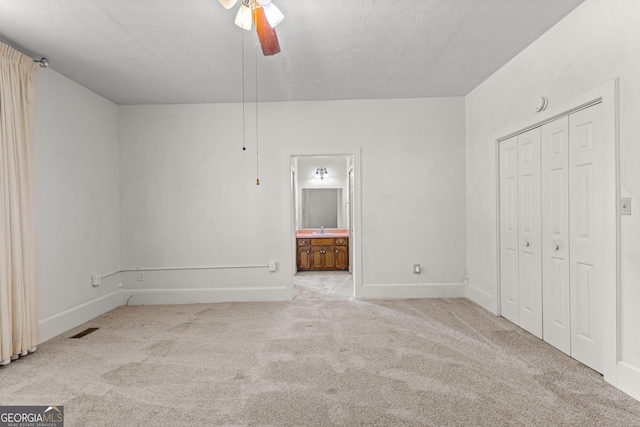 unfurnished bedroom with a textured ceiling, connected bathroom, light carpet, ceiling fan, and a closet