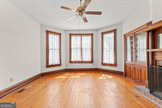 interior space with a fireplace, ceiling fan, and light hardwood / wood-style floors