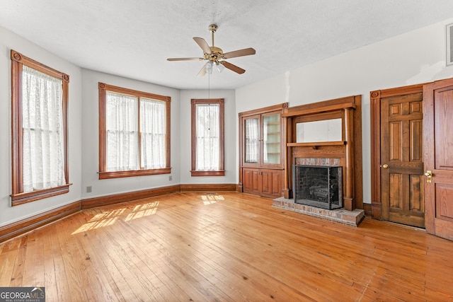 unfurnished living room featuring a brick fireplace, ceiling fan, light hardwood / wood-style floors, and a healthy amount of sunlight