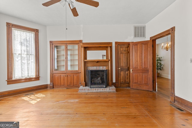 unfurnished living room featuring light wood-type flooring, a brick fireplace, and ceiling fan with notable chandelier