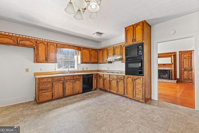 kitchen with black appliances, a brick fireplace, a textured ceiling, an inviting chandelier, and sink