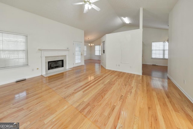 unfurnished living room with vaulted ceiling, ceiling fan with notable chandelier, a fireplace, and light wood-type flooring