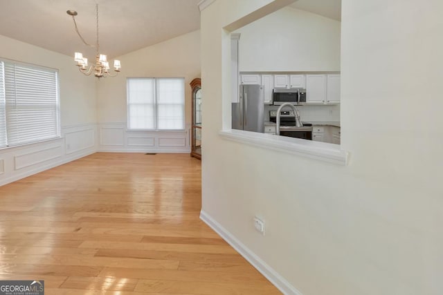 unfurnished dining area featuring lofted ceiling, a notable chandelier, and light hardwood / wood-style flooring