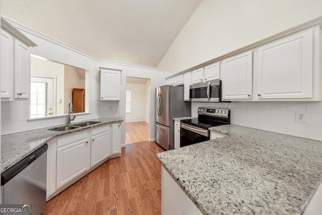 kitchen featuring sink, white cabinetry, light stone counters, vaulted ceiling, and appliances with stainless steel finishes