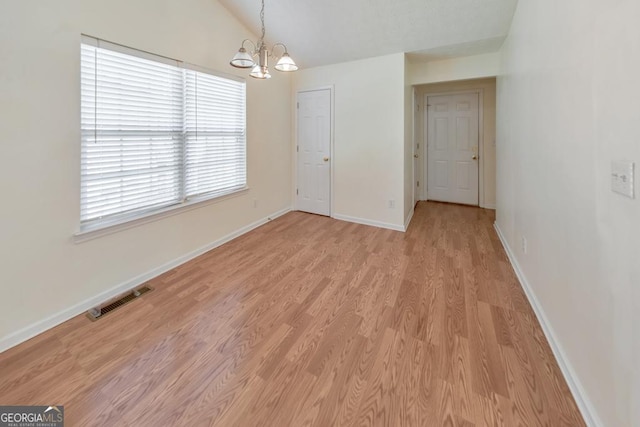 spare room featuring lofted ceiling, a notable chandelier, and light hardwood / wood-style flooring