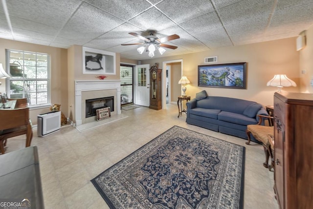 living room with a drop ceiling, a fireplace, and ceiling fan