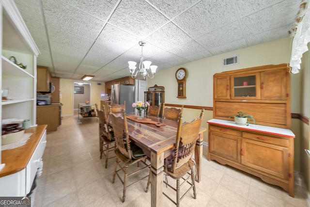 dining space with a drop ceiling and a notable chandelier